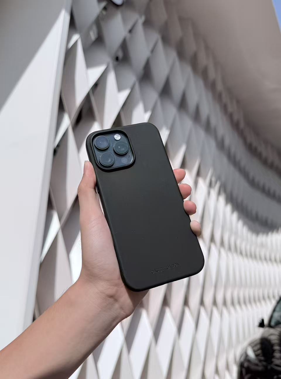 Hand holding a black silicone iPhone 16 pro case against a geometric wall background